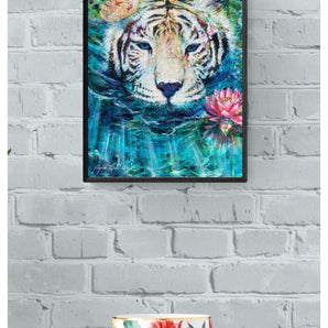 Framed painting of a white tiger swimming in clear blue water with water lilies. It hangs on a white wall above a table.